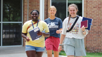 Three students smiling walking out of a dorm with their Jump Start Day packets in hand. 