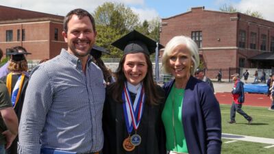 A student smiling with her parents after graduation. 