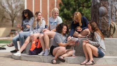 A group of students hanging out by the creation sculpture at the center of quad. 