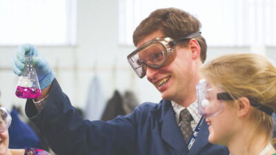 A science professor examining a liquid in a beaker with a student during a lab.