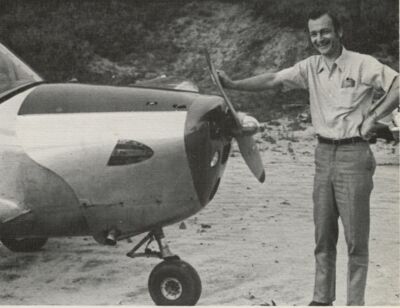 Charles Krutz smiling next to a small airplane while resting his hand on the propeller. 