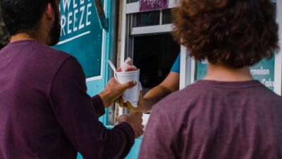 A food truck employee handing someone a snow cone through the order window. 