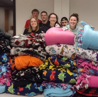 Bulldogs for Life members standing in front of a pile of fleece blanket they made. 