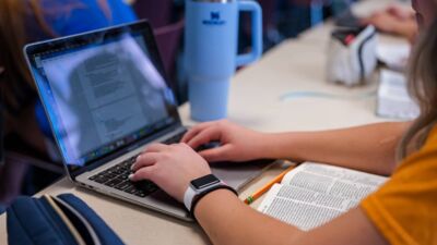 A student typing notes in class with her Bible open in front of her. 