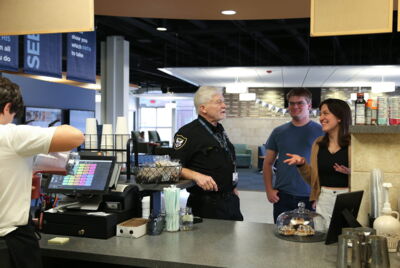 A security guard chatting with two students in line at 10:31 Coffee Shop.