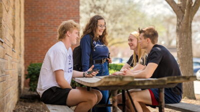 Four students gathered at a picnic table outside a dorm. 