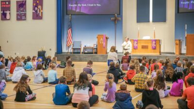 Grade school students sitting on the gym floor during a chapel service. 